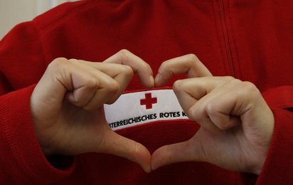 © ÖRK/Ursula Fraisl Frau formt mit Händen ein Herz. Im Hintergrund ist das Logo des Österreichischen Roten Kreuzes erkennbar